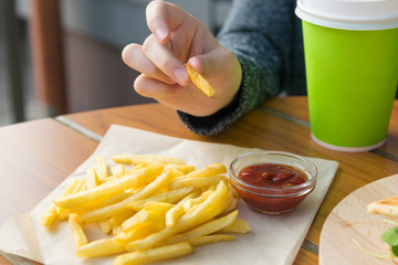 children's hand holds a slice of french fries, on the table is a portion of potatoes and ketchup