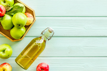 Apple cider in bottle near tray with fruits on green wooden background top view copy space