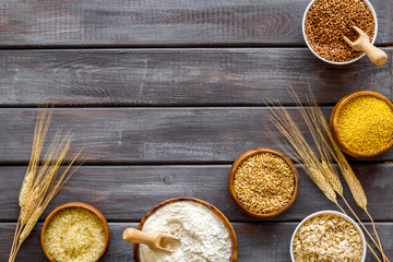 Set of cereals - rice, oats, buckwheat - in bowls with ears on dark wooden background top view frame copy space