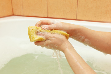 Female hands soaping a yellow sponge in the bathroom