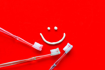 Teeth health concept. Smile drawn with toothpaste near toothbrushes on red background top view copy space