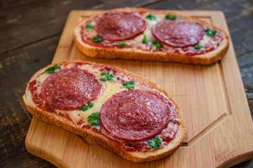 open sandwiches with salami sausage cheese tomato sauce pepperoni pizza style  on wooden board close up