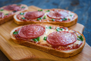 hot open sandwiches with salami cheese tomato sauce pepperoni pizza style  on wooden board close up