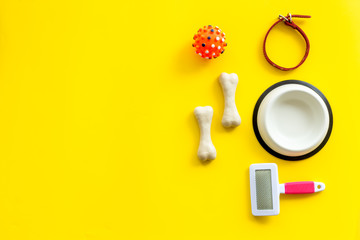 Pet's accessories like bones, collar and bowl on yellow background top view flat lay frame copy space