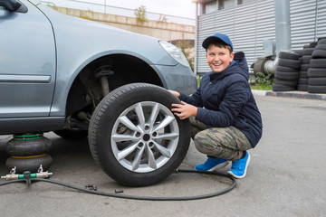 Fototapeta na wymiar Children's auto mechanic changes the wheel on a car. Wheel repair.