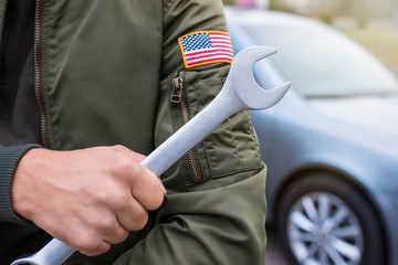 Car mechanic holds a wrench on the background of the car. Auto repair concept, lifestyle.