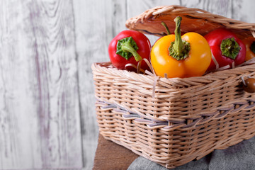Fototapeta na wymiar Little red and yellow bell peppers in a wicker basket against white wooden background
