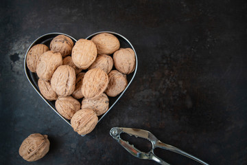 Walnuts in heart shaped cookie cutter and nutcracker on grunge old metal background 