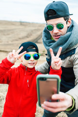 young father with his son having fun outside in spring field, happy family smiling, lifestyle people making selfie wearing sunglasses