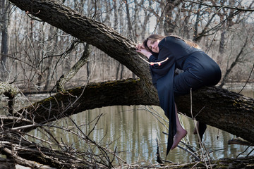 Woman with dark long hair in black robes hanging on tree branches in the middle of a swamp. Halloween and Gothic concept. Witchcraft and magic. Witch.