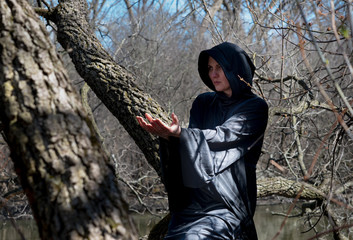 Woman with dark long hair in black robes hanging on tree branches in the middle of a swamp. Halloween and Gothic concept. Witchcraft and magic. Witch.