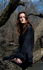 Woman with dark long hair in black robes hanging on tree branches in the middle of a swamp. Halloween and Gothic concept. Witchcraft and magic. Witch.