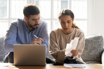Serious couple calculating expenses, bills together, using laptop