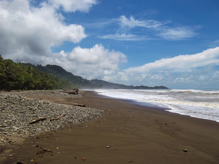 Fototapeta na wymiar Landscape of sandy beach in Colombian natural park, over Caribbean sea with waves and jungle vegetation. A sunny day with clouds. Tayrona National Park