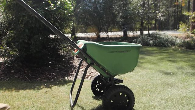 Man fertilizing and seeding residential backyard lawn with manual grass fertilizer spreader.