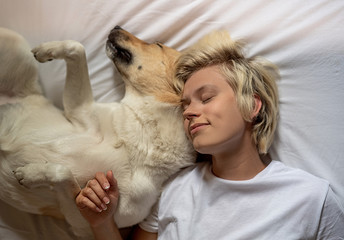 Happy blond woman laying in bed with her shepherd dog