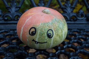 Pumpkin with a funny face painted on a black wrought iron bench close up