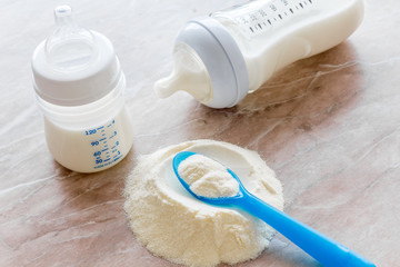 Baby food. Powder in spoon near baby bottle on brown background