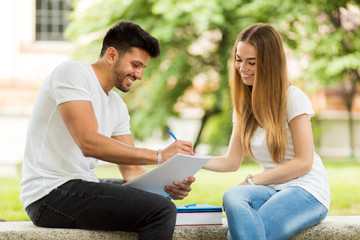 Two students studying together sitting on a bench outdoor