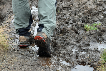 Close up of man's hiking boots and lower trousers, hiking through mud outdoors