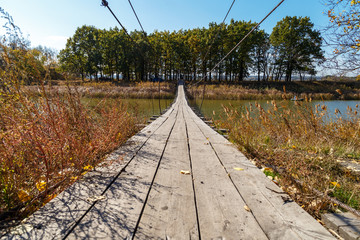 Wooden cable bridge across the river on a sunny autumn day.