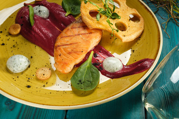 Baked salmon fillet with tomato sauce and cream sauce in bags decorated with greens and edible chips on an orange plate standing on a blue background