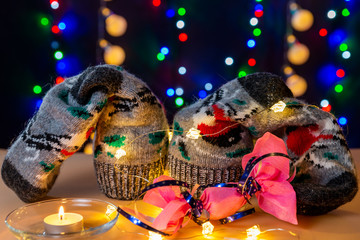 Present socks, lights, glowing candle and pink candy with blue ribbon are on the light table/background. There are different colors lights (red, green, blue, gold) on the background. Merry Christmas. 