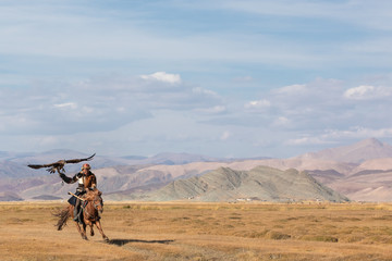 Kazakh eagle hunter galloping with his golden eagle. Ulgii, Western Mongolia.