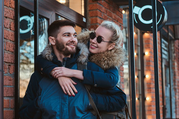 Attractive blond woman in sunglasses is hugging her handsome man on the street.