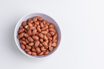 Raw shelled whole peanuts in a white bowl, isolated on white background, soft light, copy space