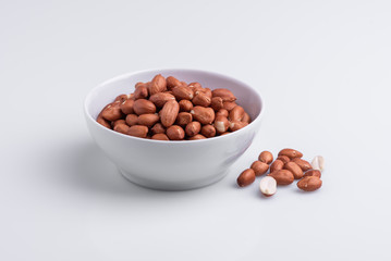 Raw shelled whole peanuts in a white bowl, isolated on white background, soft light, copy space