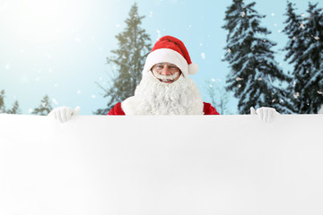 Santa Claus with blank poster in winter forest
