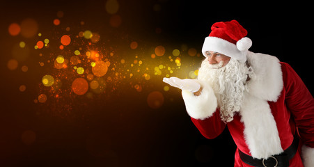 Santa Claus blowing glowing lights on dark background