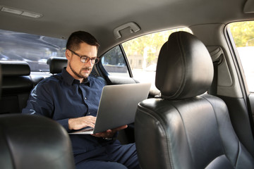 Successful businessman with laptop in modern car
