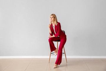 Beautiful stylish businesswoman sitting on chair against light wall