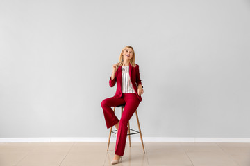 Beautiful stylish businesswoman sitting on chair against light wall