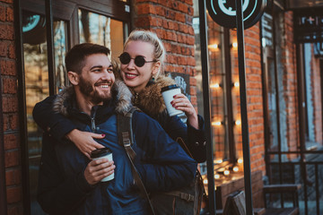 Cheerful smiling couple is enjoying their coffee outside cozy cafeteria, woman is hugging her man.