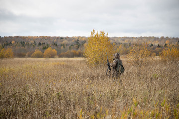 The hunter is walking across the field, with weapons. Next to the dog is a springer spaniel. Autumn