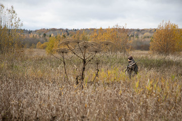 The hunter is walking across the field, with weapons. Next to the dog is a springer spaniel. Autumn