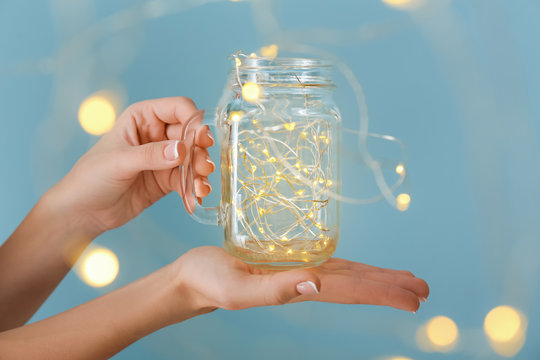 Female hands with glowing garland in jar on color background - Powered by Adobe