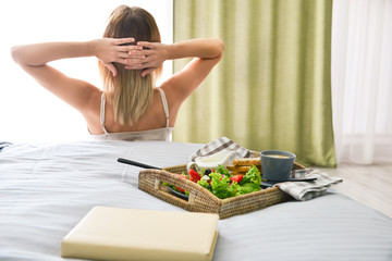 Obraz na płótnie Canvas Tray with tasty breakfast on bed of young woman
