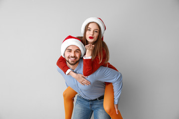 Happy young couple in Santa hats on light background