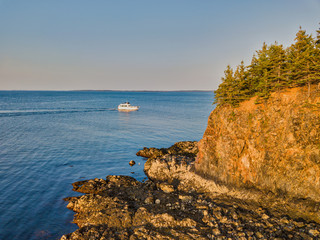 Aerial drone image of a cabin cruiser leaving owl head harbor at sunset near the rocky cliffs at low tide
