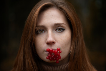  Red-haired girl with skin covered with bright freckles, with a sprig of red viburnum on her lips close-up