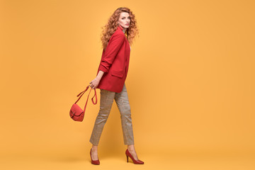 Fototapeta na wymiar Fashion. Beautiful woman in autumn red jacket, trendy curly hair, make up. Adorable well dressed redhead girl on orange. Gorgeous fashionable lady in red, hairstyle, makeup. Creative beauty shot