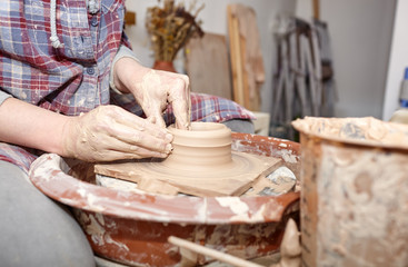Potter working on potters wheel making ceramic pot from clay in pottery workshop
