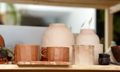 Beautiful closeup of ceramic cups and pots on wooden plank in pottery workshop.Brown pottery from clay