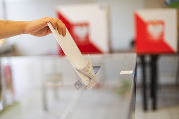Throwing a card with a vote.to the ballot box during  elections. In the backround polish arms and flag - obrazy, fototapety, plakaty
