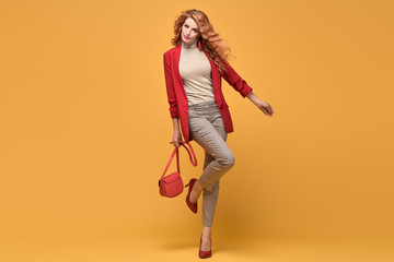 Fototapeta na wymiar Fashionable woman in Trendy autumn spring outfit, stylish wavy hair, makeup. Joyful lady in red jacket smiling dance on orange. Cheerful girl, stylish fashion accessories, beauty style
