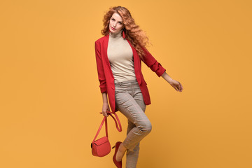 Fashionable woman in Trendy autumn spring outfit, stylish wavy hair, makeup. Joyful lady in red jacket smiling dance on orange. Cheerful girl, stylish fashion accessories, beauty style